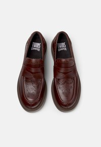 Dunkelbraune Lederschuhe mit dekorativen Brogue-Details, abgerundeter Form, elastischem Riemen und gepolsterter Innensohle.