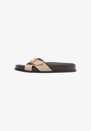 Sandale slide marron avec une lanière en daim beige croisée et une boucle dorée sur une semelle plate noire.