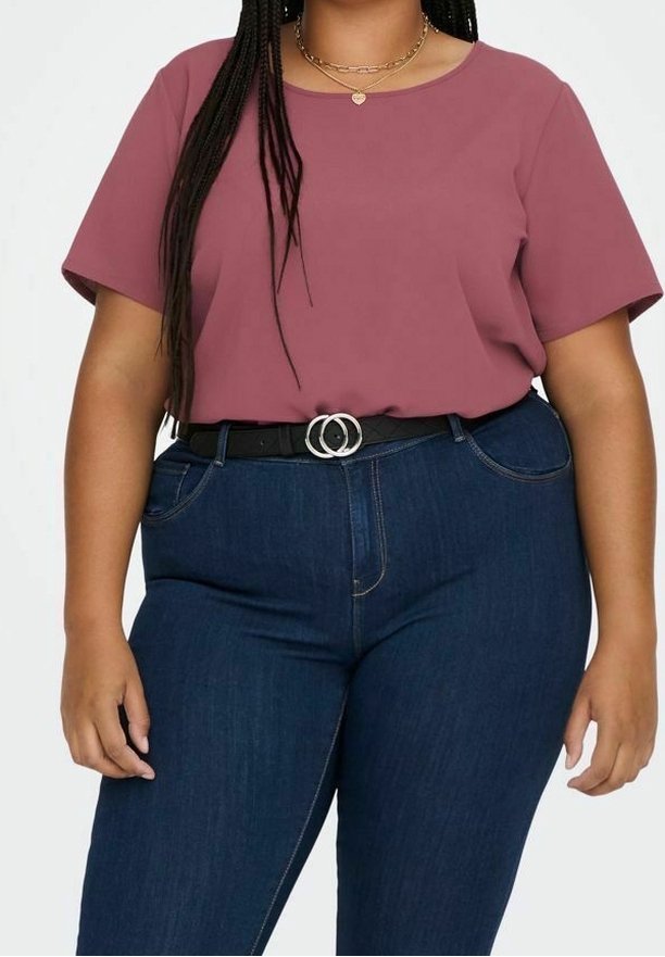 Femme portant un chemisier mauve à manches courtes, rentré dans un jean bleu foncé taille haute avec une ceinture noire dotée d'une boucle à double anneau.