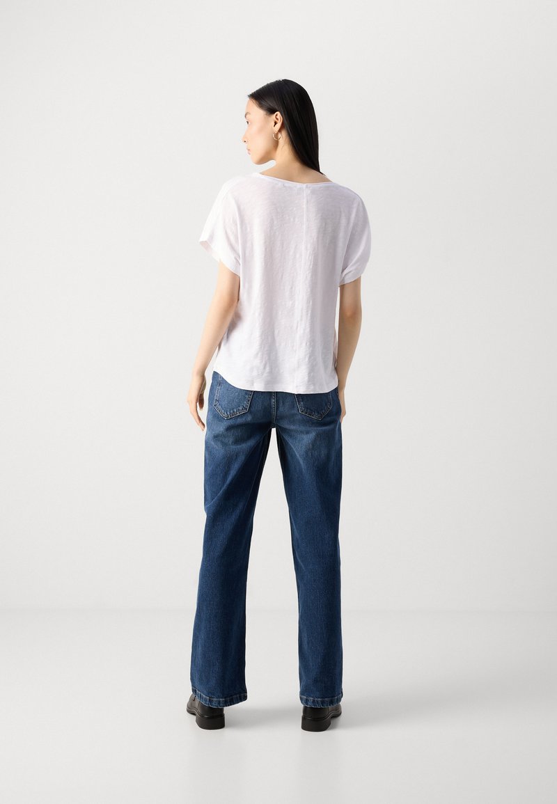 Biała bluzka z krótkim rękawem o luźnym kroju, zestawiona z dżinsami w kolorze niebieskim z wysokim stanem. Strój ma prosty, codzienny design.