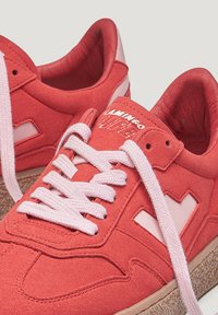 Baskets en daim rouge avec des lacets roses, semelles en caoutchouc et accents blancs. Présente un logo sur la languette et des détails texturés sur la tige.