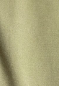 Tissu vert olive clair avec une texture lisse, présentant un motif de tissage subtil. Le matériau semble durable et a un doux éclat.