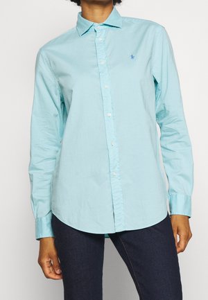 Jasnoniebieska koszula na guziki z długimi rękawami, ostrym kołnierzykiem i subtelnym logo na piersi. Wykonana z gładkiej bawełnianej tkaniny.