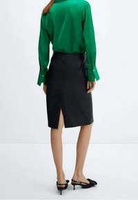 Jupe crayon noire avec une fente au dos, associée à un chemisier vert brillant. La tenue présente des lignes épurées et une coupe ajustée.