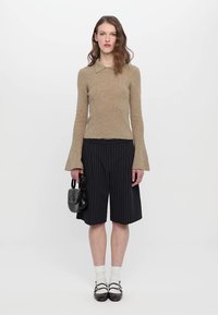 Beige ribbestrikket genser med krage, kombinert med svarte pinstripe shorts. Modellen holder en liten svart håndveske, iført hvite sokker og svarte sko.