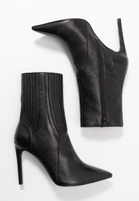 Pari musta nahka korkokengät nilkkurit, joissa on terävät varpaat ja sivuvetoketjut, esitelty valkoisella taustalla.