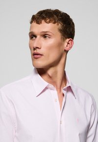 Lichtroze gestreepte shirt met een button-down kraag, met subtiele textuur en een klein logo op de linkerkant van de borst.