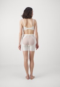 White lingerie set featuring a sheer back panel and smooth finish. The bodysuit has a mid-thigh cut with contrasting textures and clean lines.