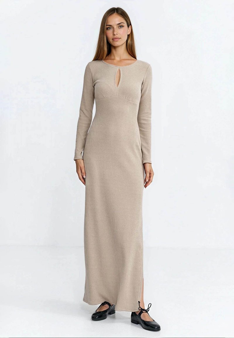 Beżowa, długorękawowa, prążkowana sukienka z wycięciem w kształcie łezki przy dekolcie i bocznymi rozcięciami, zestawiona z czarnymi płaskimi butami.