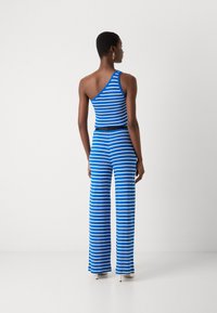 Blå och vit randig one-shoulder jumpsuit med vida byxor och en åtsittande midja. Slät tyg med en texturerad yta.