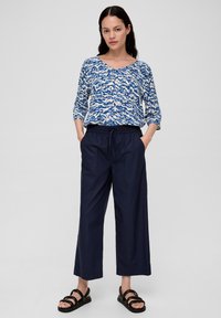 Blauw-witte blouse met een V-hals en driekwart mouwen, gecombineerd met marineblauwe broek met wijde pijpen en zwarte sandalen met bandjes.