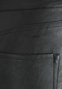 Zwarte leren kledingstuk met een gestructureerd oppervlak, horizontale naden en een enkele zak met zichtbare steekdetails.