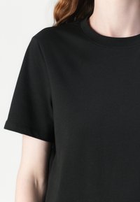 Crna pamučna T-majica s kratkim rukavima i okruglim izrezom. Tkanina izgleda glatko, a kroj je udoban. Nema vidljivih uzoraka ili detalja.