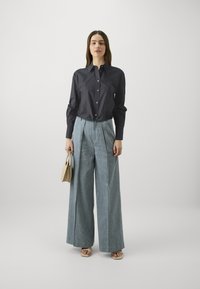 Μαύρο πουκάμισο με κουμπιά και μακριά μανίκια, συνδυασμένο με τζιν παντελόνια σε ίσια γραμμή με ψηλή μέση. Μια μπεζ τσάντα και σανδάλια ολοκληρώνουν την εμφάνιση.