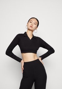 Top cropped preto de malha com decote em V e mangas compridas, combinado com calças pretas de malha de cintura alta, apresentando um discreto logo.