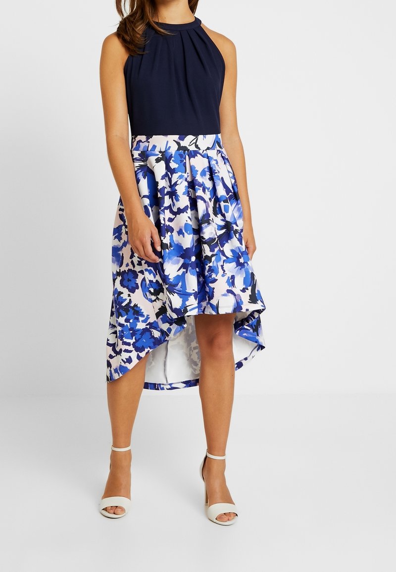 Sukienka na szyję z granatowym topem i spódnicą we wzory kwiatowe w niebiesko-białe odcienie, z asymetrycznym dołem i zwiewnym materiałem.