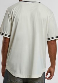 Kremowa koszula z krótkim rękawem wykonana z teksturowanej tkaniny, z czarnym paskowanym kołnierzem i mankietami, z zaokrąglonym dołem i luźnym krojem.