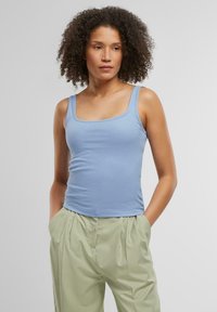 Top de tirantes de canalé azul claro con un escote cuadrado, combinado con pantalones sueltos de pliegues verdes claros. La tela parece suave y elástica.