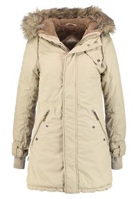 Cappotto imbottito beige con cappuccio in pelliccia sintetica, chiusura con zip frontale, due tasche laterali e polsini a coste. Presenta una fodera testurizzata e una vita abbastanza aderente.