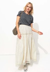 T-shirt gris à manches roulées avec un motif en forme de cœur, assorti d'une jupe maxi blanche brodée. Les accessoires comprennent un sac à imprimé léopard et des baskets.