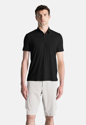 Polo shirt nero a maniche corte con colletto alla coreana, texture liscia, logo discreto sul petto, abbinato a pantaloni corti beige chiaro.