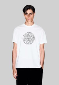 T-shirt in cotone bianco con una grafica circolare in nero che elenca vari nomi di città sul davanti. Maniche corte, collo rotondo.