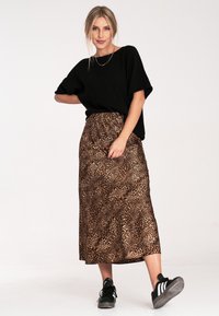 Czarna, oversize koszulka, midi spódnica w wzór panterki w odcieniach brązu, gładki materiał, luźny krój. Czarne buty sportowe z białymi paskami.