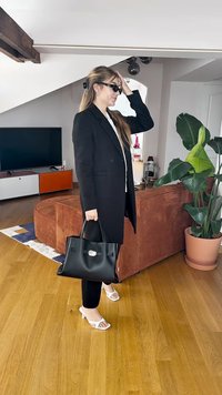 Sort blazer, hvid top, sort håndtaske med sølvbeslag, sorte leggings og hvide sandaler på trægulv. Indendørs omgivelser med plante.