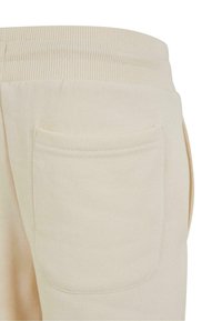 Imagine detaliată cu pantaloni bej care arată talia elastică și un buzunar rectangular cusut în partea din spate, pe un material moale.