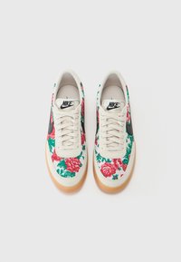 Biele tenisky s kvetinovým vzorom v červenej a zelenej farbe, s čiernym vzorom a gumovou podrážkou. Textúrovaný textilný zvršok.