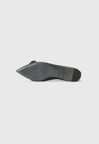 Chaussure à talon haut noire avec un bout pointu, un dessus en cuir lisse et une semelle en caoutchouc texturée. Présente un accent de boucle décorative sur le côté.