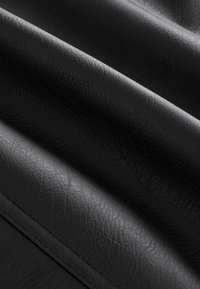Fekete műbőr textil, texturált felülettel, hajtott részekkel, amelyek kiemelik sima fényét és finom redőit.