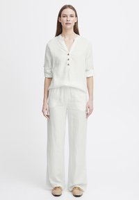 Ensemble en lin blanc comprenant un haut à col et à boutons et un pantalon ample. Le tissu a une texture douce, avec un design décontracté.