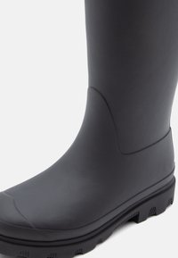 Black rubber boot with a smooth texture, rounded toe, and raised tread on the sole. Ankle-height with a seamless design and minimal accents.