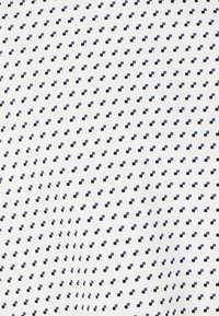 Tissu à motifs en blanc avec de petites formes géométriques bleues et noires, créant un design en grille uniforme sur l'ensemble du matériau.