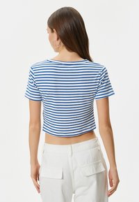 Korta t-shirt med blå och vita horisontella ränder, ribbat mönster, rundad halsringning, korta ärmar, tillsammans med vita byxor.