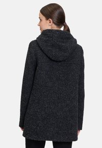 Czarny, strukturalny wełniany płaszcz z kapturem, luźny krój i prosty dół. Widoczne szwy i miękkie wykończenie. Widok z tyłu.