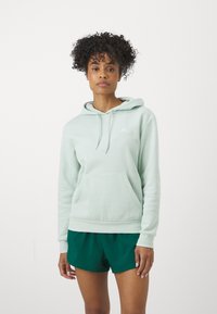 Hoodie verde claro com um bolso frontal, capuz com cordão e detalhe do logotipo branco no peito, combinado com calções verdes escuros.