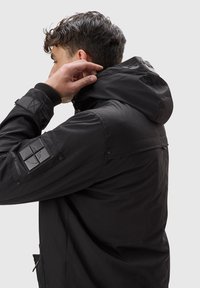 Svart vattentät jacka med huva, med texturerade lappar på ärmarna, tryckknappsstängningar och en elegant, minimalistisk design.