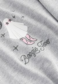 Grå stof med et grafik af en hvid figur i en kappe med pink detaljer og sølvstjerner. Teksten siger "Boogie Fever" i sølv.