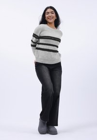 Helles graues Sweatshirt mit schwarzen Streifen, kombiniert mit dunklen Jeans und grauen Stiefeln. Das Sweatshirt hat einen Rundhalsausschnitt und eine weiche Textur.