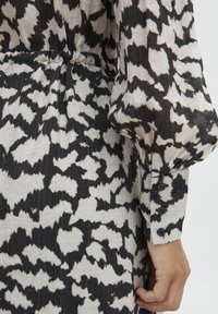 Vestito a righe in bianco e nero con un tessuto strutturato, caratterizzato da maniche lunghe e un polsino bottonato, arricciato in vita.