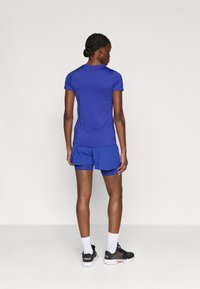 Top deportivo azul royal de manga corta combinado con pantalones cortos azules a juego. Llevado con zapatillas deportivas negras y blancas y calcetines de tobillo.