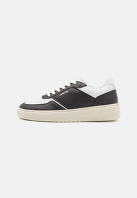 Sneaker con tomaia in pelle nera, dettagli in pelle bianca, punta perforata e suola in gomma beige. Design con lacci per una vestibilità sicura.