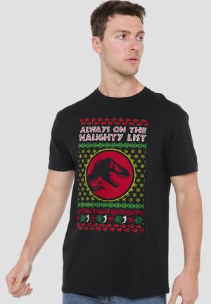 Man wearing black T-shirt with red and green holiday-themed design and text "Always on the Naughty List" featuring a dinosaur head silhouette.