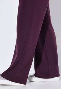 Paarse wijde broek gemaakt van zachte stof, gecombineerd met witte sneakers met een sprankelende metallic teenaccent.