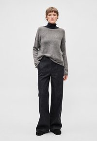 Szary, oversize'owy sweter z szerokim dekoltem, zestawiony z ciemnymi spodniami o szerokich nogawkach. Tkanina wydaje się miękka z delikatną fakturą.