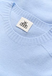 Hele sinine kudumissärk, millel on soonikkoes kaelus ja pehme tekstuur. Krae sisse on õmmeldud valge silt musta logoga.