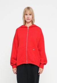 Felpa rossa con zip realizzata in morbido misto cotone, dotata di tasca frontale e accento con logo bianco. Presenta un fit rilassato e un ampio cappuccio.