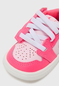 Pink sneaker featuring smooth synthetic upper, white lace closure, perforated toe box, and rubber sole. Accents of darker pink on the design.